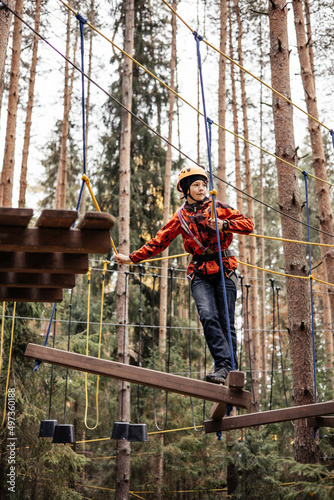 Teenager boy in safety equipment routing and climbing in adventure rope park. Child in helmet climbing trees in an extreme park. Outdoor activities. Active lifestyle