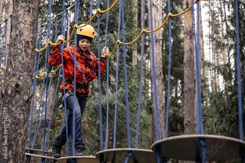 Teenager boy in safety equipment routing and climbing in adventure rope park. Child in helmet climbing trees in an extreme park. Outdoor activities. Active lifestyle