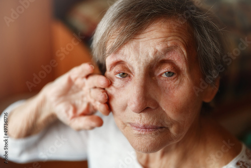 Senior lonely woman sitting at home and looking at camera. Old woman is crying and wipping away tears
