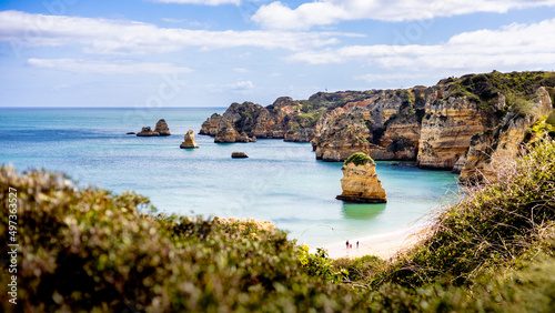 View of Praia de Dona Ana beach with cliffs and sand in Lagos, Algarve, Portugal. Three persons walking along the beach.