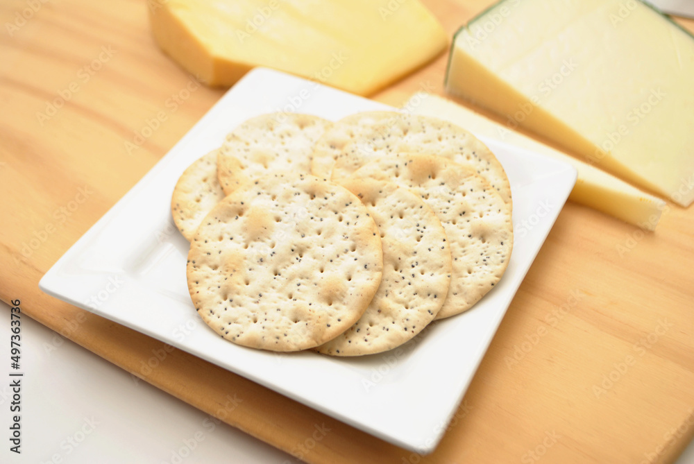 Sesame Crackers on a Wooden Cutting Board with Gourmet Cheeses and a Knife in the Background Sesame Crackers on a Wooden Cutting Board with Gourmet Cheeses and a Knife in the Background