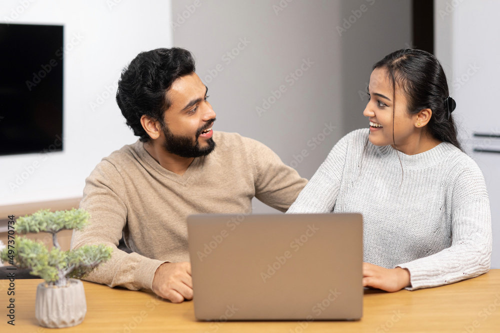 Video call with friends. Cheerful married couple using laptop for video connection. Wife and husband are waiving into webcam with smiling while sitting at the table at cozy room Video call with friends. Cheerful married couple using laptop for video connection. Wife and husband are waiving into webcam with smiling while sitting at the table at cozy room