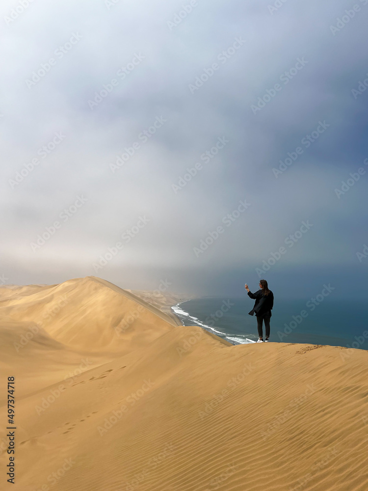 A young woman stands sandy dunes on seashore. Sandwich Harbour in Namibia.