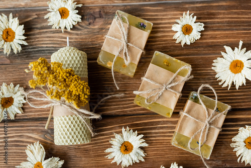 Top view of craft candle and soap near dry flowers on wooden surface.