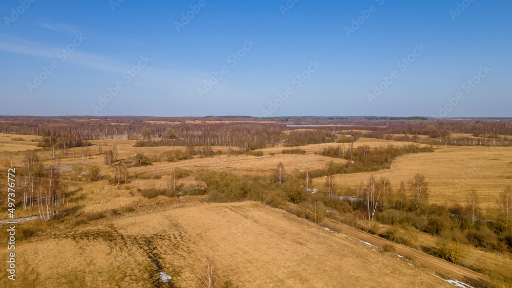 Aerial view of fields with copse, dry yellow grass, a stream, remnants of snow in early spring. Nature background.