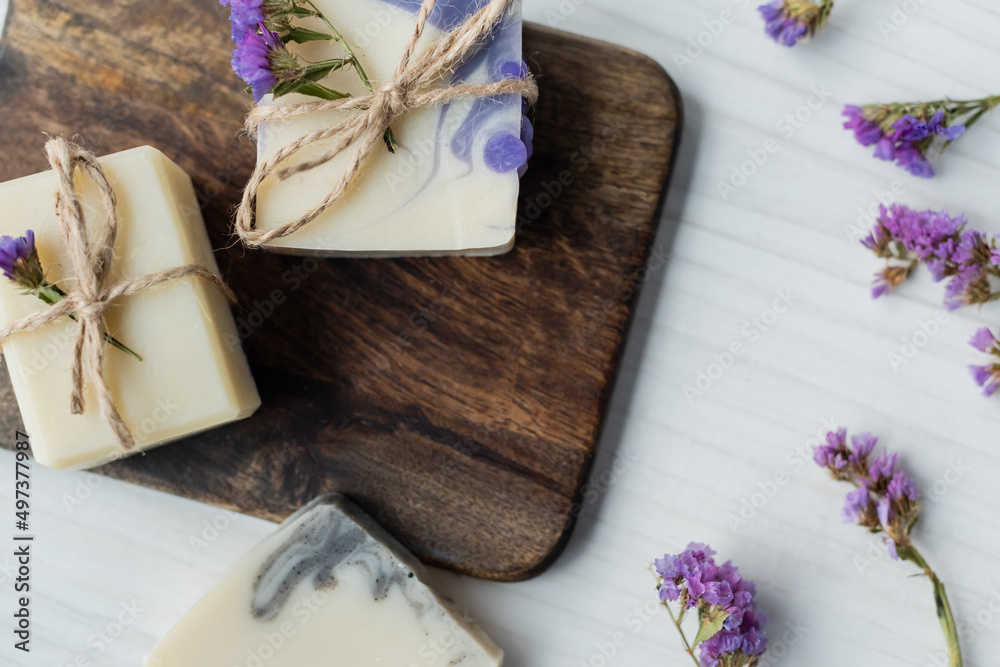 Fototapeta premium Top view of handmade soap bars on cutting board near dry flowers on table.