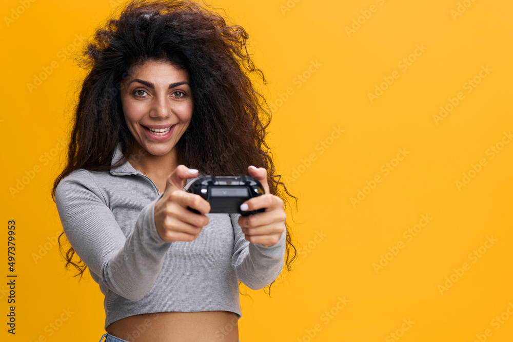 Young fun excited satisfied happy joyful woman 20s with afro hair wearing gray t-shirt hold in hand play pc game with joystick console isolated on pastel orange color background studio portrait. Young fun excited satisfied happy joyful woman 20s with afro hair wearing gray t-shirt hold in hand play pc game with joystick console isolated on pastel orange color background studio portrait.
