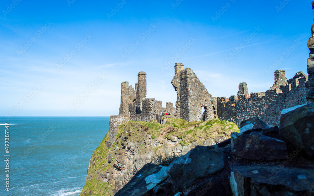 Famous Dunluce Castle on the cliff with blue sea background in a sunny day.