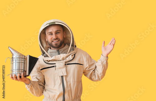 Fototapete Male beekeeper in protective suit with smoker on yellow background