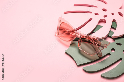 Stylish sunglasses and decorative palm leaves on color background