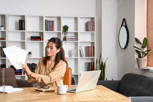 Young Asian tutor with paper sheets giving lesson online at home