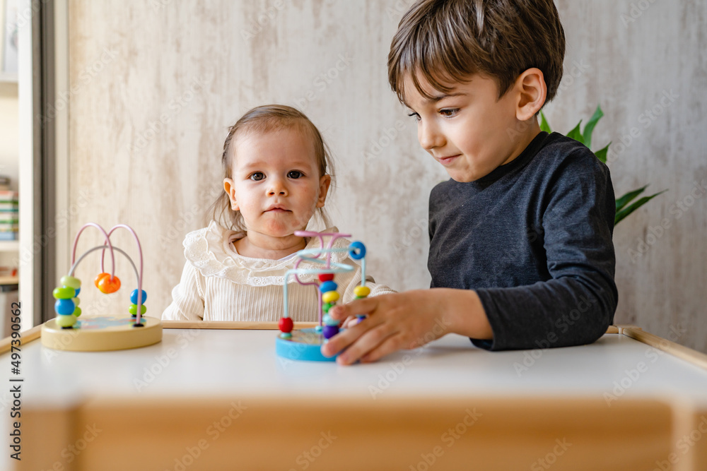 Fototapeta premium Brother and sister playing at home siblings children baby girl and five years old boy play with toys in bright room in day front view copy space family life concept growing up