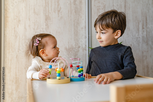 Brother and sister playing at home siblings children baby girl and five years old boy play with toys in bright room in day front view copy space family life concept growing up