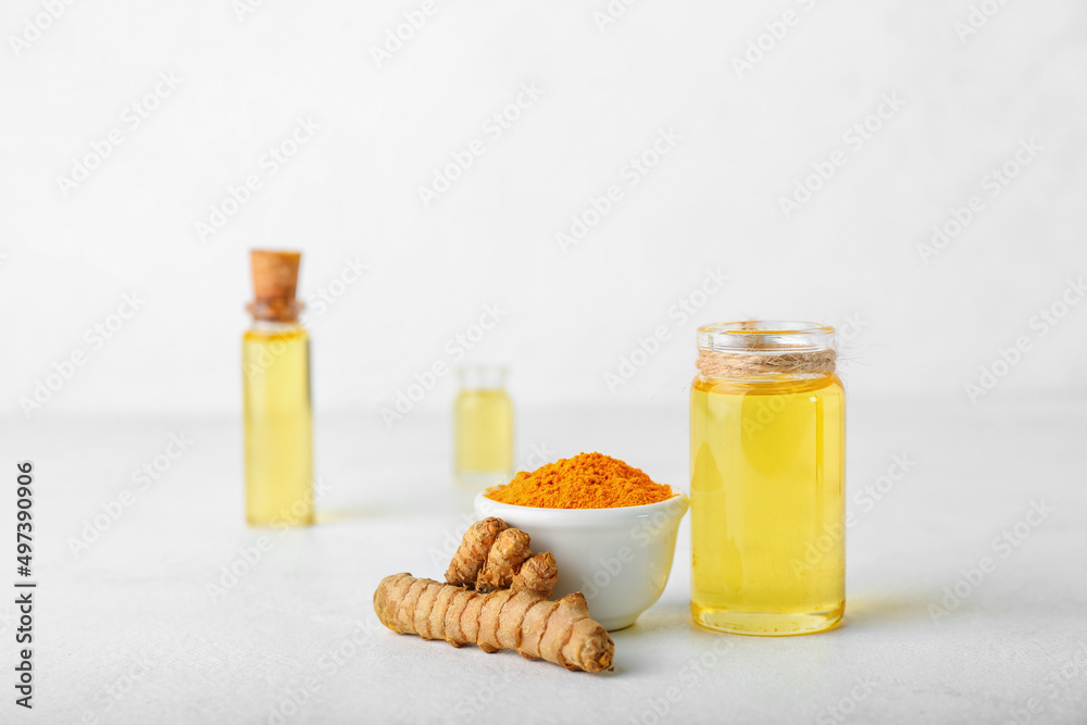 Bottle of oil, turmeric root and bowl with powder on light background Bottle of oil, turmeric root and bowl with powder on light background