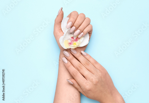 Woman with beautiful manicure holding orchid flower on blue background  closeup