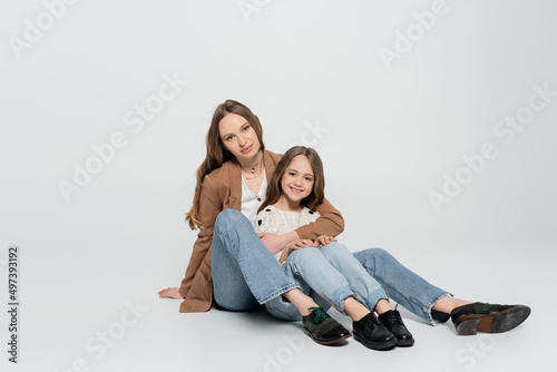 full length view of mother and child in trendy clothes sitting on grey background.