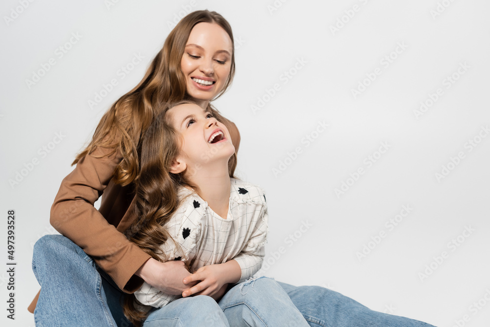 happy woman embracing laughing daughter isolated on grey.