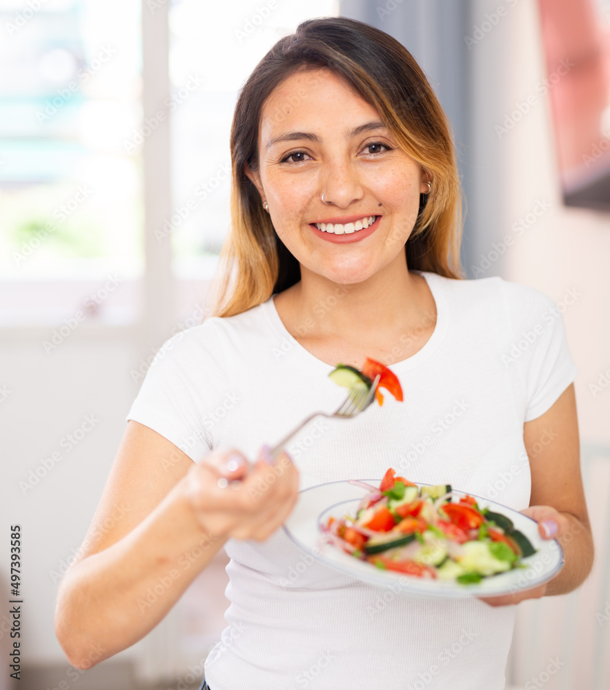 Portrait of colombian housewife eating vegetable salad at table at home
