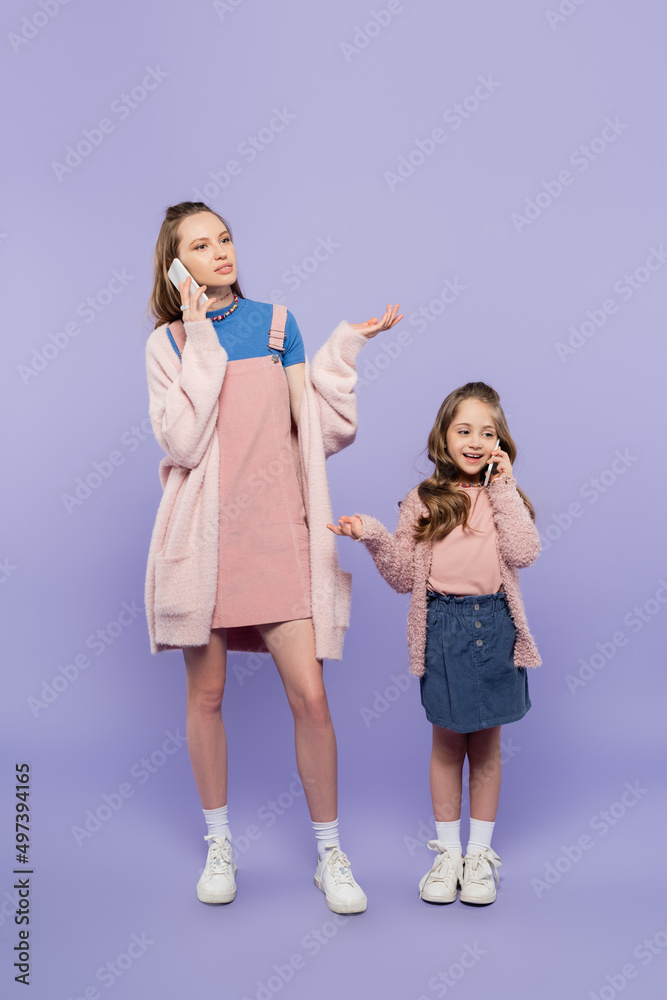 full length of mother and daughter talking on mobile phones while gesturing on purple. full length of mother and daughter talking on mobile phones while gesturing on purple.