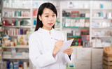 Chinese woman pharmacist keeps track of drugs in interior of pharmacy. High quality photo