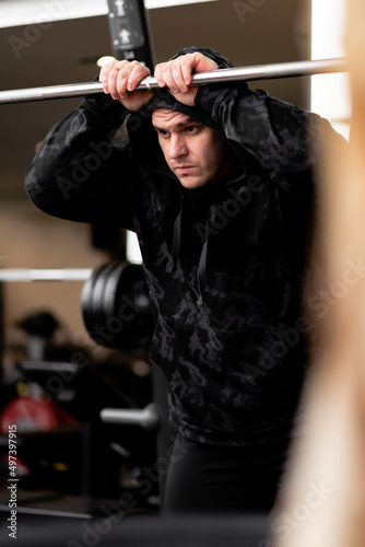 Portrait of a serious, handsome hipster man in a black hoodie or sweatshirt. Serious, young muscular sportsman is training in the gym