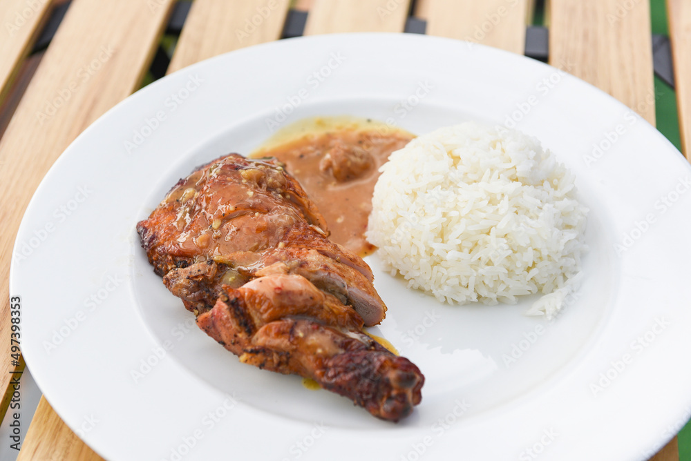 Thai rice food, cooked white rice and grilled chicken with sauce on white plate and wooden table background, Spicy bbq chicken legs grilled Thai rice food, cooked white rice and grilled chicken with sauce on white plate and wooden table background, Spicy bbq chicken legs grilled