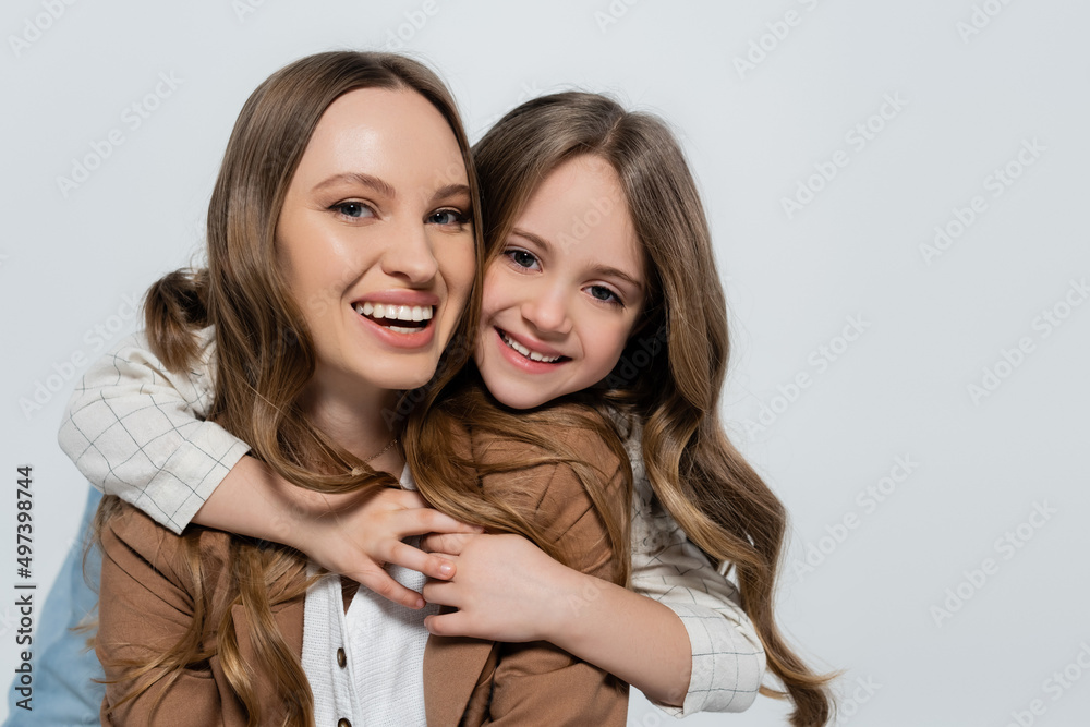 pleased girl embracing cheerful mother and looking at camera isolated on grey. pleased girl embracing cheerful mother and looking at camera isolated on grey.