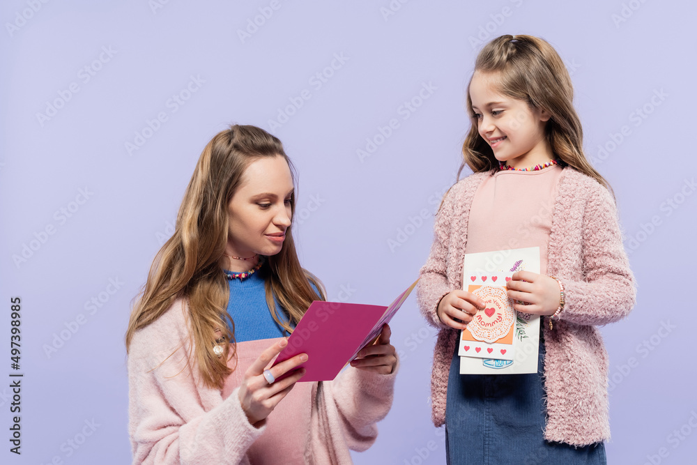 happy mother reading greeting card near cheerful daughter isolated on purple, mothers day concept. happy mother reading greeting card near cheerful daughter isolated on purple, mothers day concept.