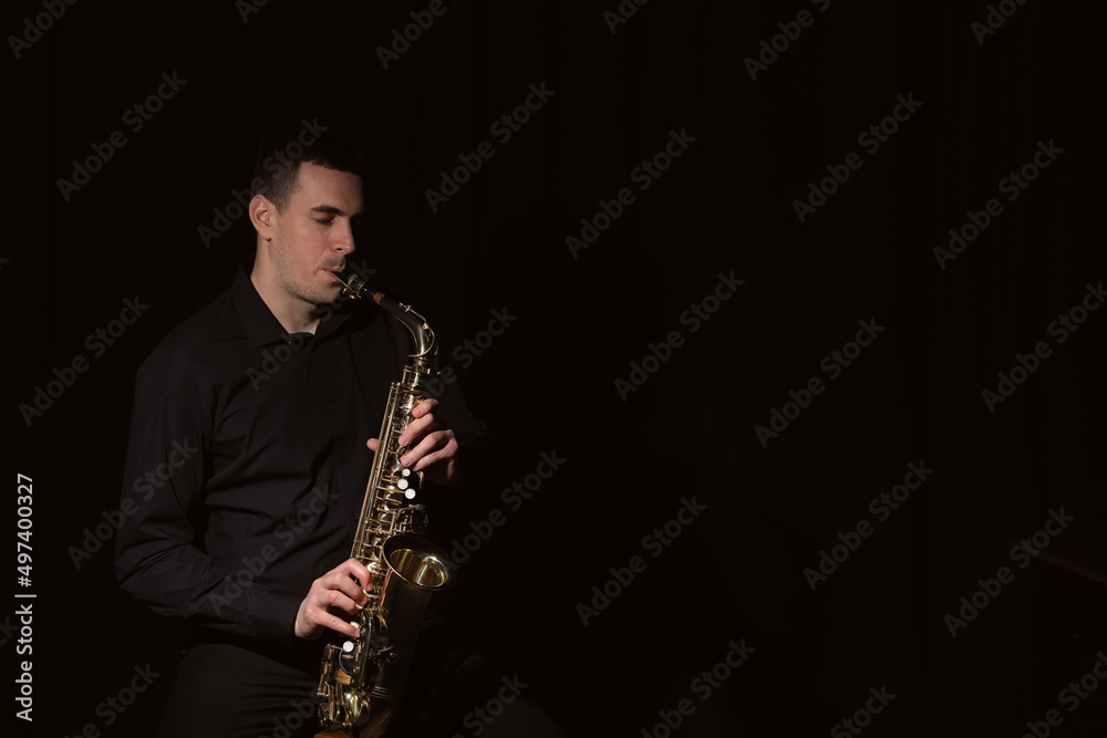 Naklejka premium Young man playing saxophone on dark background. Space for text