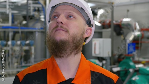 Close-up of the face of an engineer in a white helmet with a beard in the building of an industrial production workshop for pumping oil and gas condensate. Petrochemical industry