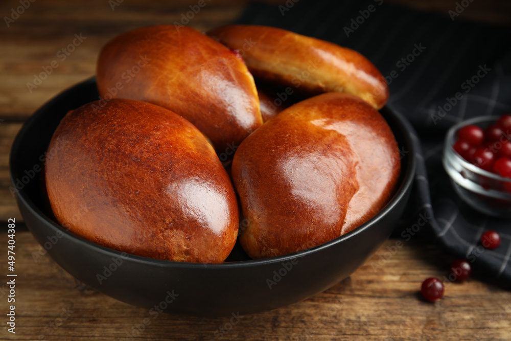 Obraz premium Delicious baked cranberry pirozhki in bowl on wooden table