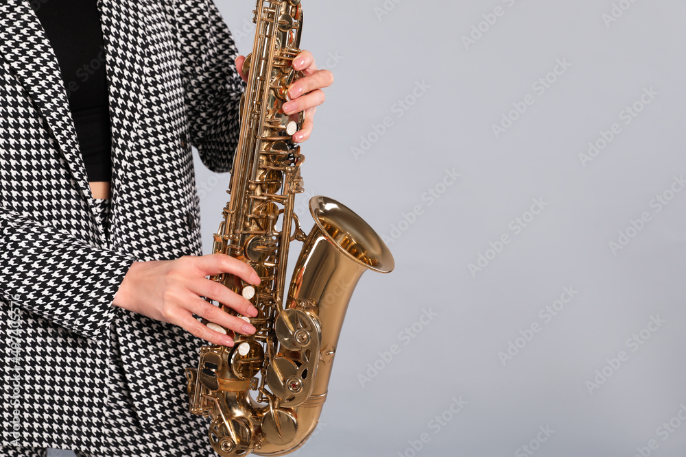 Fototapeta premium Woman in elegant suit with saxophone on grey background, closeup. Space for text