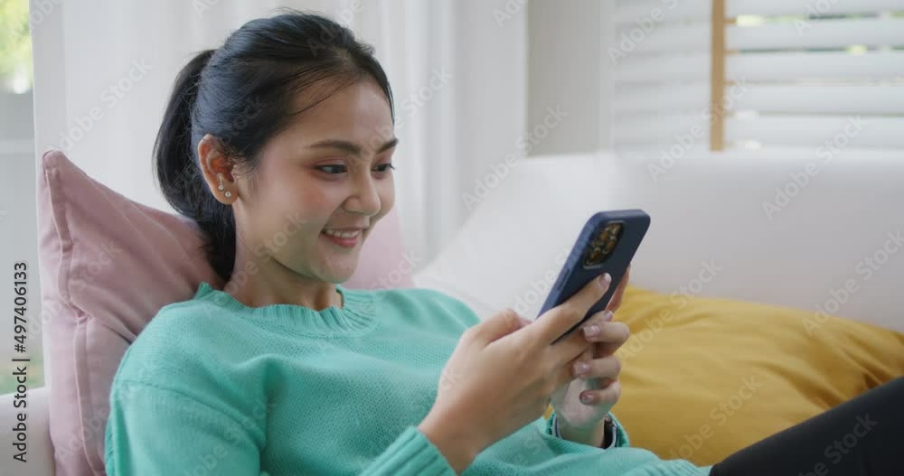 Young attractive beautiful casual asia female lady or student look at cellphone play social media IG reel tiktok app lying down at sofa couch living room feel relax comfort carefree at home apartment.