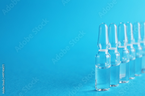 Many medical ampoules with solution on light blue background. Space for text