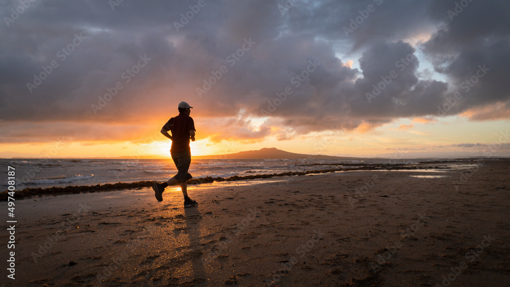 Silhouette man running on Takapuna beach at sunrise, Rangitoto Island in the background, Auckland.