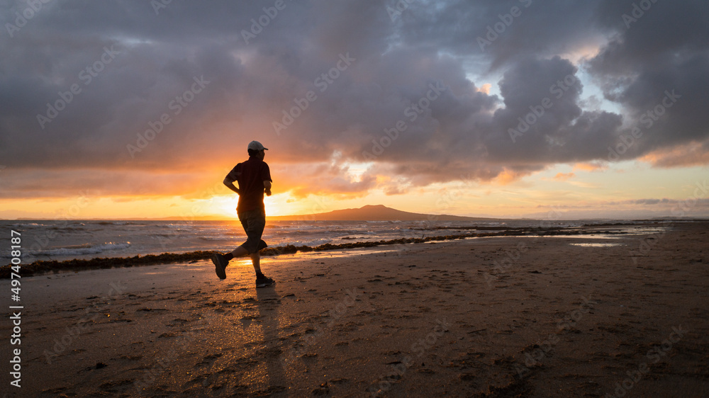 Silhouette man running on Takapuna beach at sunrise, Rangitoto Island in the background, Auckland. Silhouette man running on Takapuna beach at sunrise, Rangitoto Island in the background, Auckland.