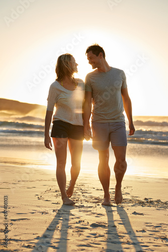 Im so happy that I can lean on him. Shot of a couple walking closely together on the beach at sunset.