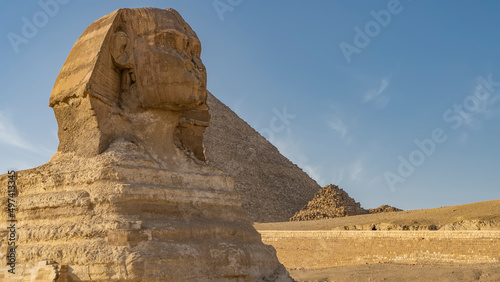 Sculpture of the Great Sphinx against the blue sky and the pyramid of Menkaure. The head is visible  the face is close-up  the layered structure of sandstone. Egypt. Giza Plateau