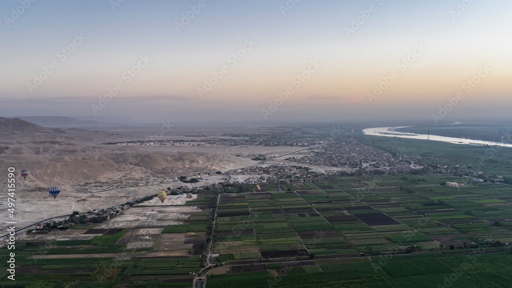 Aerial view of the Nile Valley at dawn. Agricultural fields, sand dunes, river beds, flying balloons are visible. The morning sky is bluish-pink. Egypt. Luxor