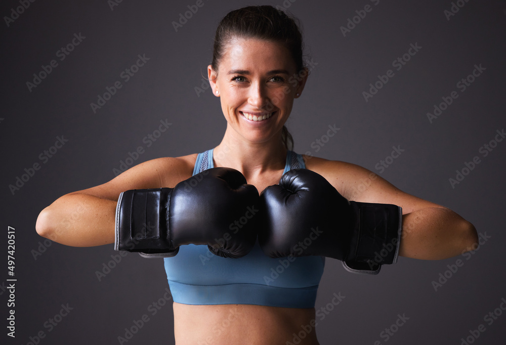 Wanna see how much power are in my punches. Portrait of a young woman wearing boxing gloves against a grey background.