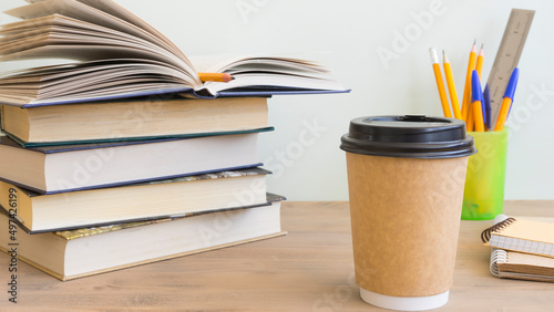 Coffee in a paper cup and a stack of books next to it