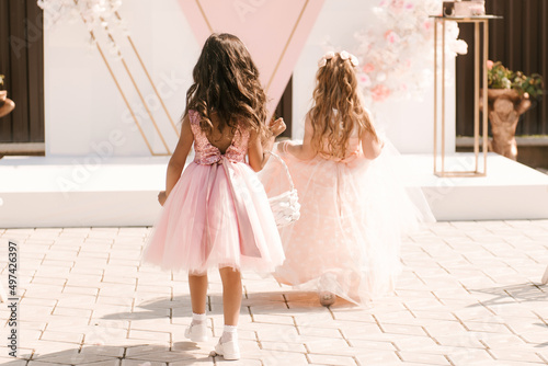 Obraz na płótnie Little beautiful girls in puffy dresses eat petals and rings at the wedding, back view w salonie
