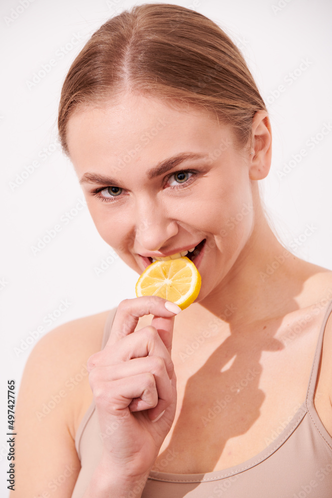beautiful blonde woman laying on a white wooden background next to slices of lemon, having a slice of lemon on the eyes and smiling beautiful blonde woman laying on a white wooden background next to slices of lemon, having a slice of lemon on the eyes and smiling