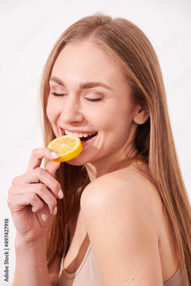 beautiful blonde woman laying on a white wooden background next to slices of lemon, having a slice of lemon on the eyes and smiling beautiful blonde woman laying on a white wooden background next to slices of lemon, having a slice of lemon on the eyes and smiling