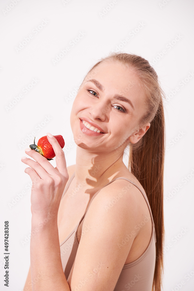 A creative portrait of a beautiful girl holding with one hand a juicy strawberry near her lips with temptation.