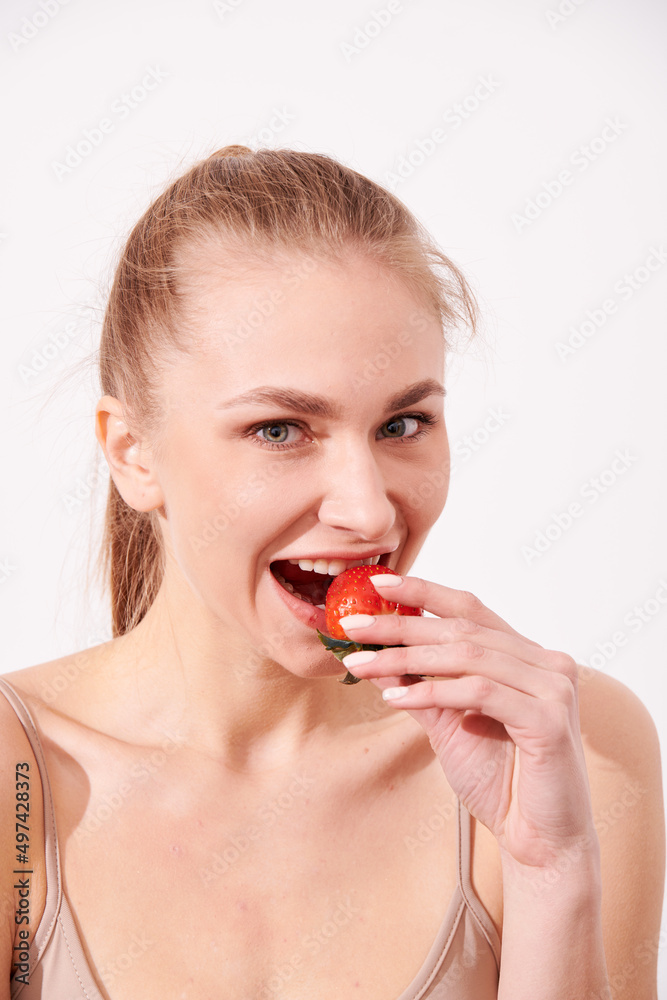 A creative portrait of a beautiful girl holding with one hand a juicy strawberry near her lips with temptation. A creative portrait of a beautiful girl holding with one hand a juicy strawberry near her lips with temptation.