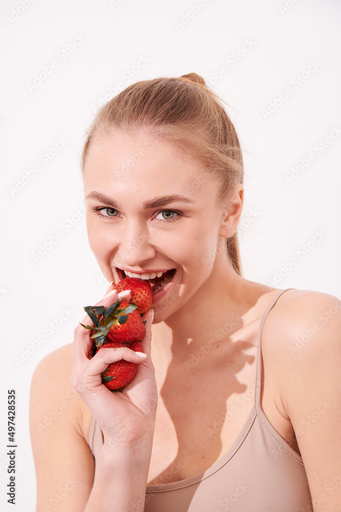 A creative portrait of a beautiful girl holding with one hand a juicy strawberry near her lips with temptation. A creative portrait of a beautiful girl holding with one hand a juicy strawberry near her lips with temptation.