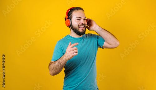 portrait of hispanic young man with headphones, dancing and listening music on yellow background in Mexico Latin America