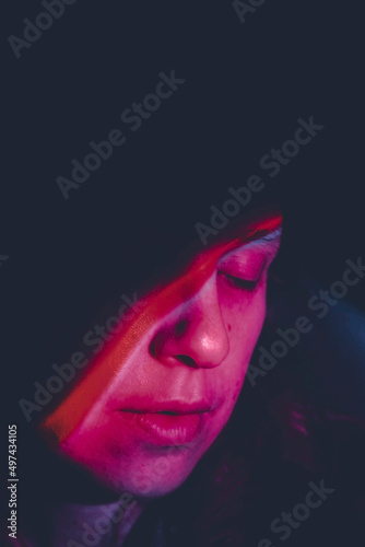 Artistic portrait of a young woman illuminated by colored lights in the dark
