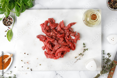 Raw chopped beef on marble cutting board with spices and oil. Cut beef into small pieces, Beef strips. Preparation food. White background photo